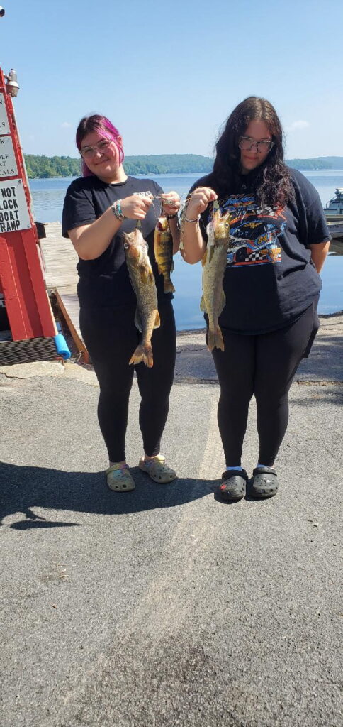 Two young girls holding out the large fish they caught with Peck's Lake in the background